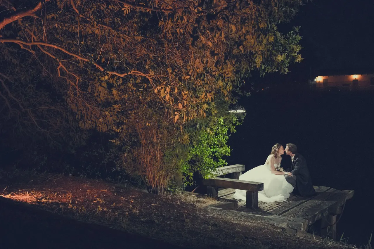 Due sposi seduti sul molo di legno sul fiume, di sera